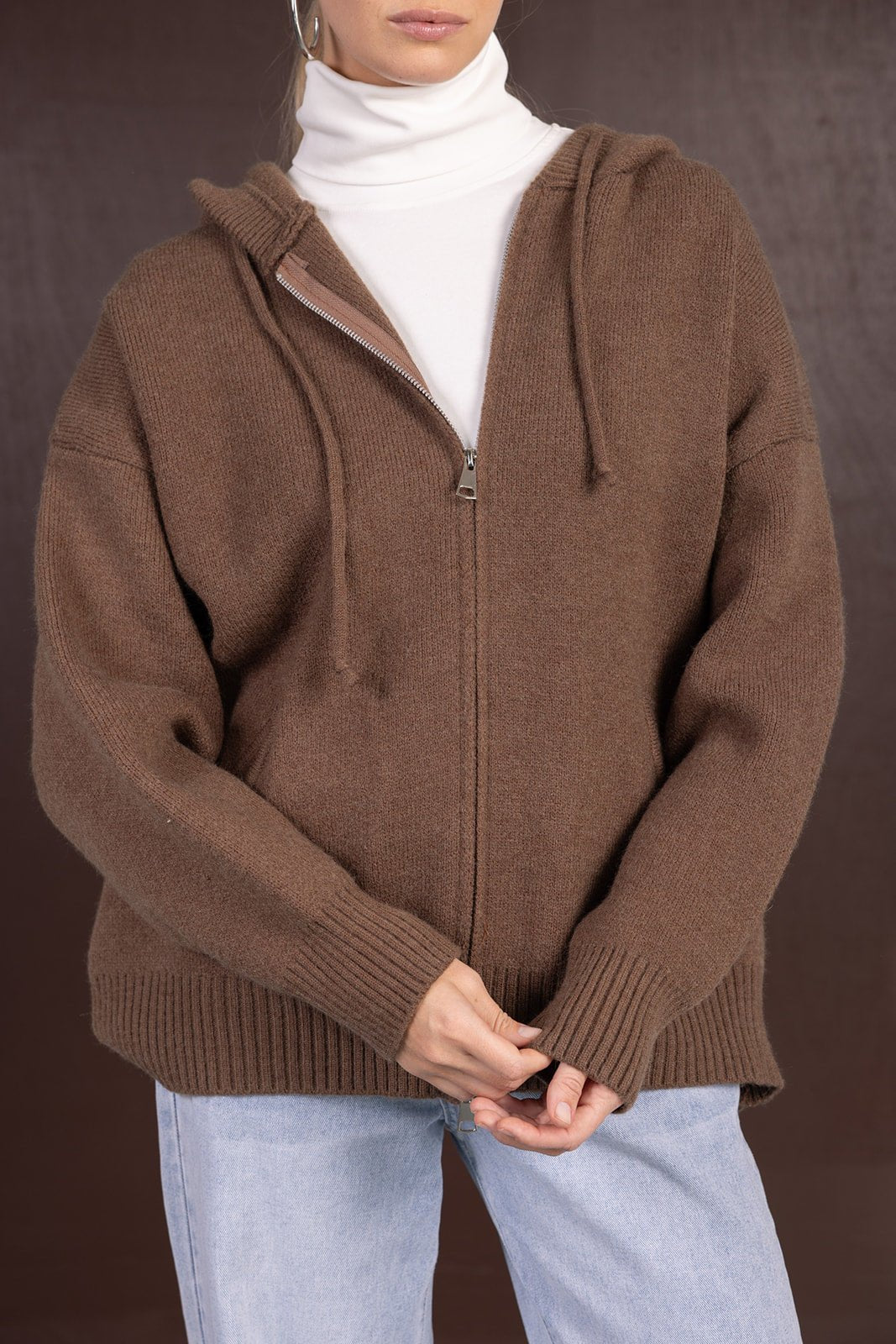 אישה לובשת סוודר קפוצ'ון חום עם רוכסן, גולף לבן ומכנסי ג'ינס אופנתיים