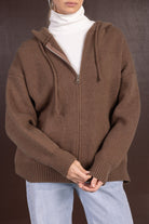 אישה לובשת סוודר קפוצ'ון חום עם רוכסן, גולף לבן ומכנסי ג'ינס אופנתיים