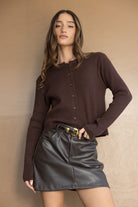 דוגמנית עם סוודר חום מכופתר וחצאית עור קצרה בגוון כהה, אופנת נשים עדכנית