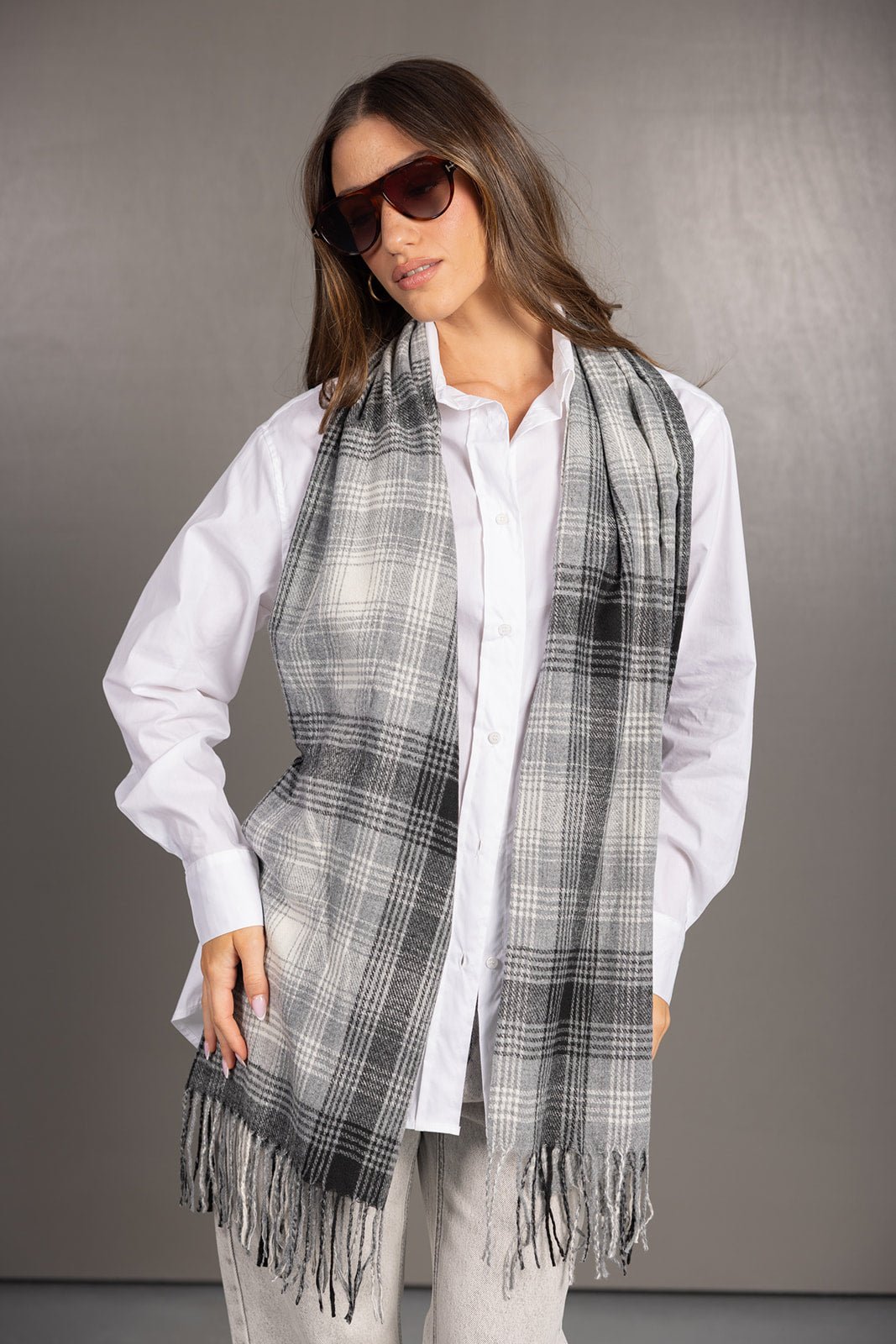 אישה לובשת חולצה לבנה וצעיף משובץ בגווני אפור עם שוליים פרומים, משקפי שמש, מראה אופנתי מודרני