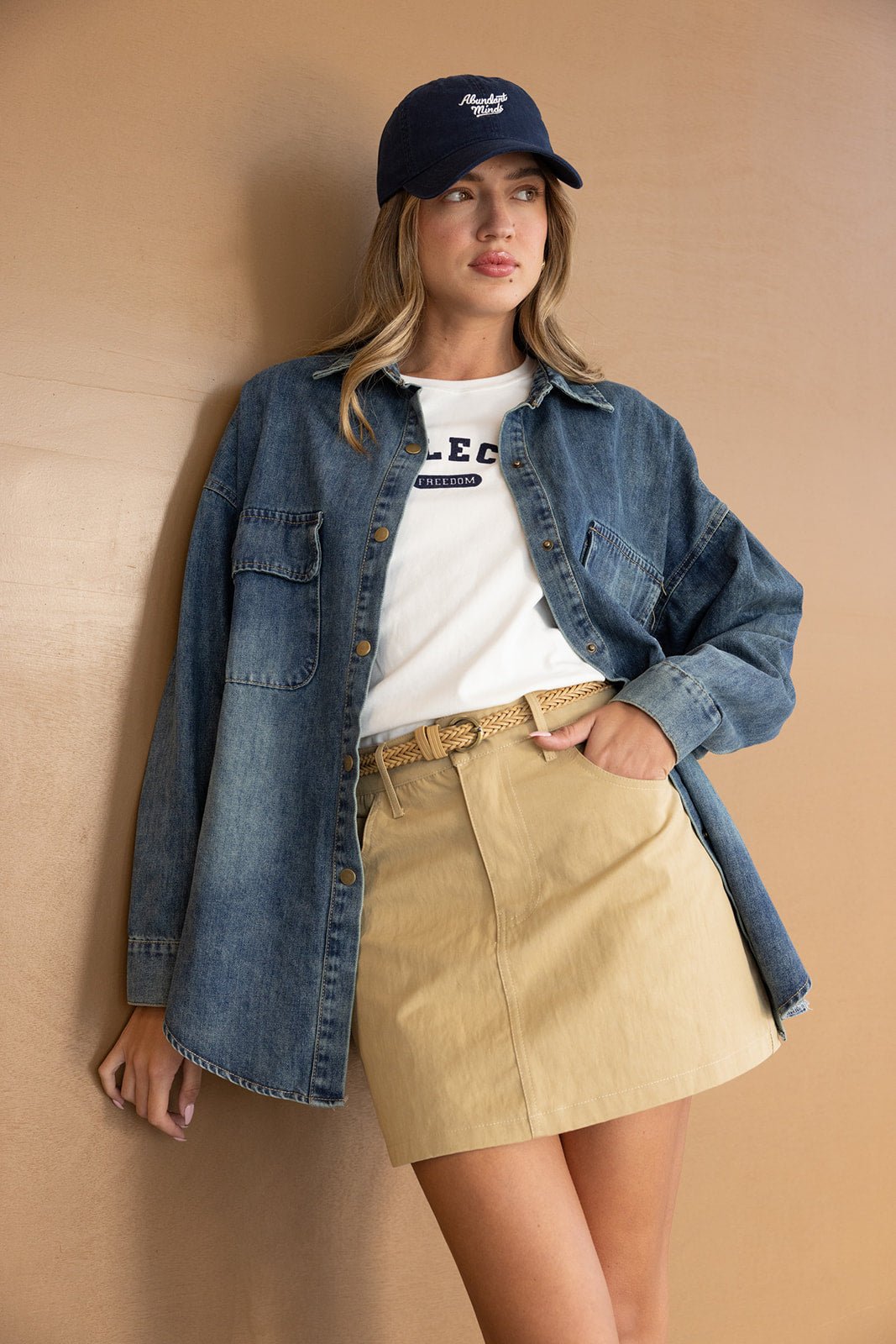 אופנת נשים קיץ: דוגמנית לובשת חצאית בז', חולצת טי לבנה, חולצה ג'ינס וכובע כחול