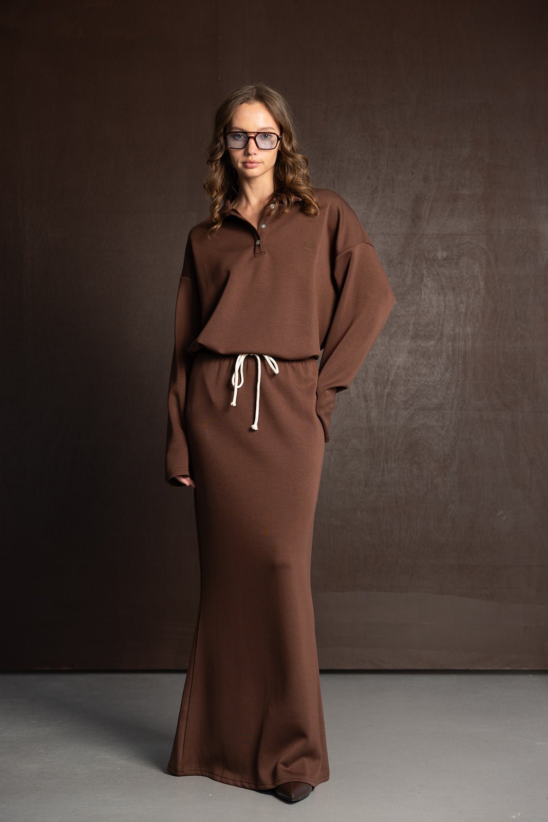 אישה לובשת שמלת מקסי חומה עם שרוך לבן, משקפי ראייה, אופנה נשית חורפית בסגנון קז'ואל