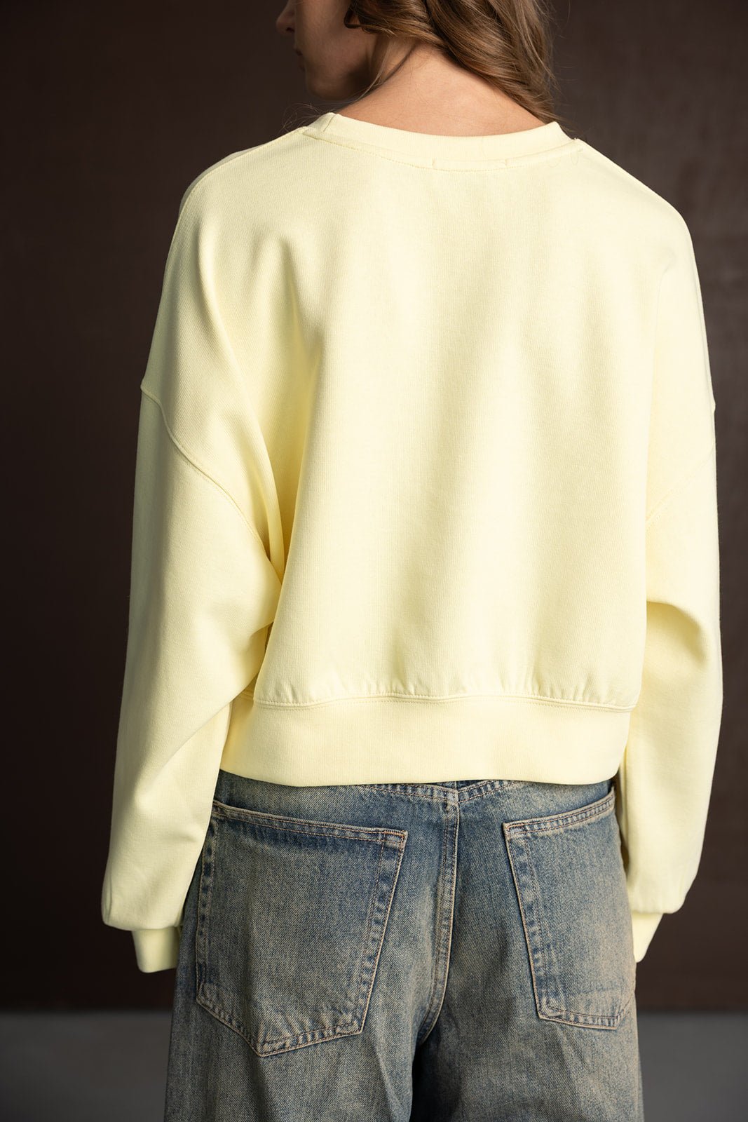 אישה לובשת סווטשירט צהוב בהיר וג'ינס בגזרה רחבה, צילום מאחור, אופנה לנשים צעירות