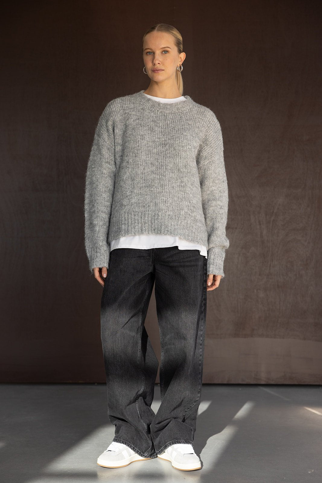 דוגמנית לובשת סוודר אפור מחמם, ג׳ינס רחב כהה ונעלי סניקרס לבנות, אופנת חורף לנשים