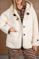 מעיל נשים חורפי לבן עם כפתורים וכיסים, חולצת פסים חומה, אופנה טרנדית לנשים צעירות