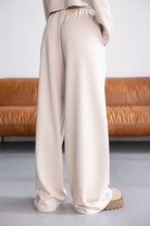 מכנסיים רחבים בגזרת ספורט בצבע בז', בד נעים, רקע ספה חומה, אופנת נשים צעירה