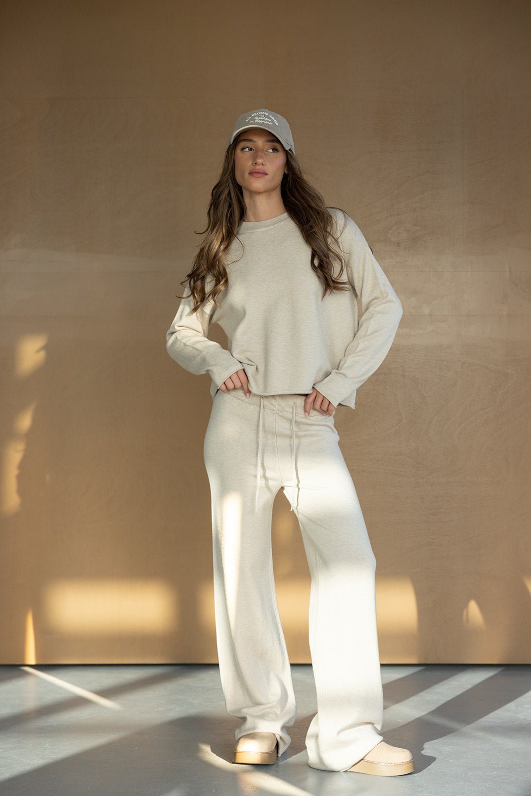 אישה עם שיער ארוך לובשת סט טרנינג בגוון שמנת וכובע מצחייה, לוק חורפי אופנתי לנשים