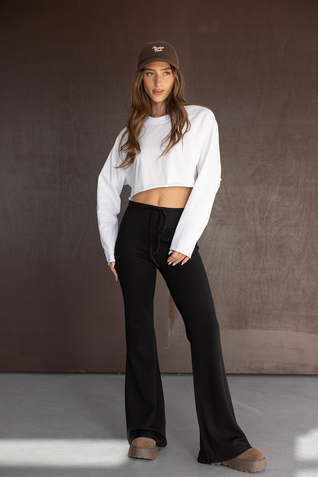 אופנת נשים, דוגמנית עם חולצת בטן לבנה, מכנסי טרנינג שחורים וכובע חום