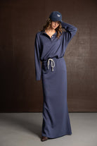 אישה לובשת שמלת ספורט ארוכה בצבע כחול כהה עם שרוך במותן וכובע, אופנת נשים עדכנית