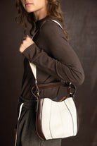 אישה עם חולצה חומה מחזיקה תיק צד אופנתי מבד לבן עם קצוות חומים, רקע כהה