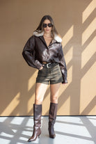 דוגמנית לובשת מעיל עור חום עם פרווה, שורטס קלאסי ומגפיים גבוהים, מראה אופנתי לנשים