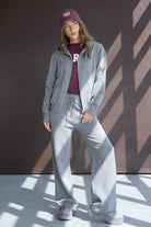 צעירה לובשת סט טרנינג אפור עם קפוצ’ון, חולצה וכובע בורדו, אופנה נינוחה לנשים