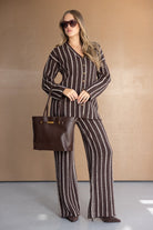 אישה לובשת חליפת נשים חורפית פסים חומה עם תיק ועקבים, משקפי שמש, לוק אופנתי בעמידה