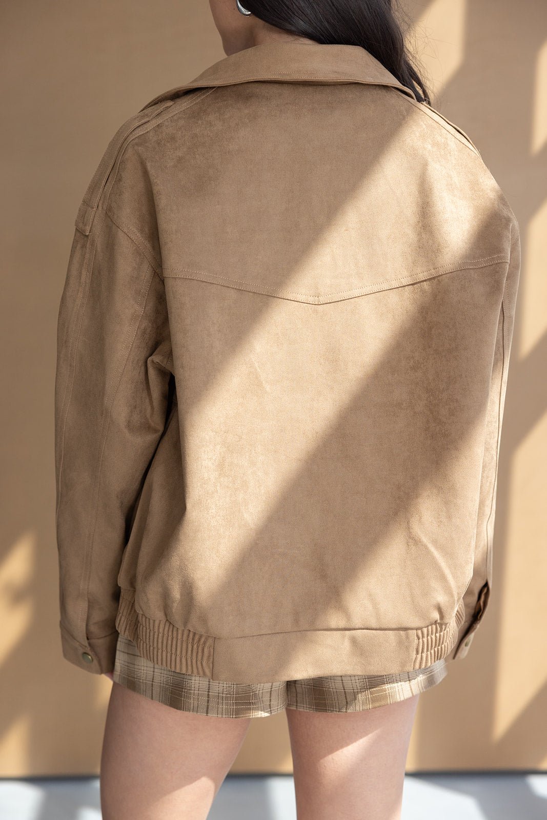 אישה לובשת ג׳קט דמוי זמש חום עם מכפלת מחורצת ומכנסיים קצרים משובצים, צילום אופנה לנשים