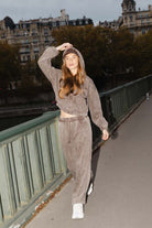 דוגמנית לובשת סט טרנינג אופנתי בצבע חום, עומדת על גשר עירוני עם בניינים ברקע