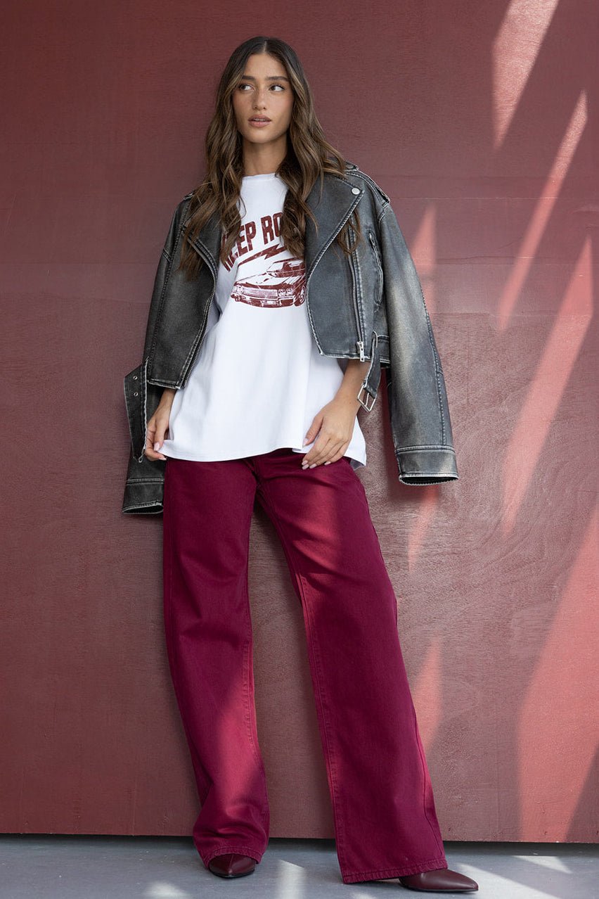 דוגמנית לובשת מכנסיים רחבים בורדו, חולצת טי לבנה עם הדפס וז'קט ג'ינס אופנתי