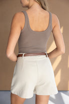 אישה לובשת גופיה קיץ חומה ומכנסיים קצרים לבנים עם חגורה חומה, צילום אופנה לנשים