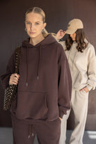 נשים עם סווצ'רים רחבים, אחת בצבע חום כהה עם תיק ניטים, שנייה בסווטשירט שמנת וכובע מצחייה אופנתי