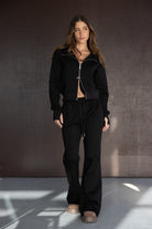 אישה לובשת סט טרנינג שחור אופנתי עם ריצ'רץ', מכנסיים מתרחבים ונעליים בצבע בז', אופנת נשים צעירה