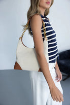 אישה עם תיק כתף קנבס אופנתי עם רצועה מוזהבת, לוק קיץ, חולצה פסים ומכנס לבן