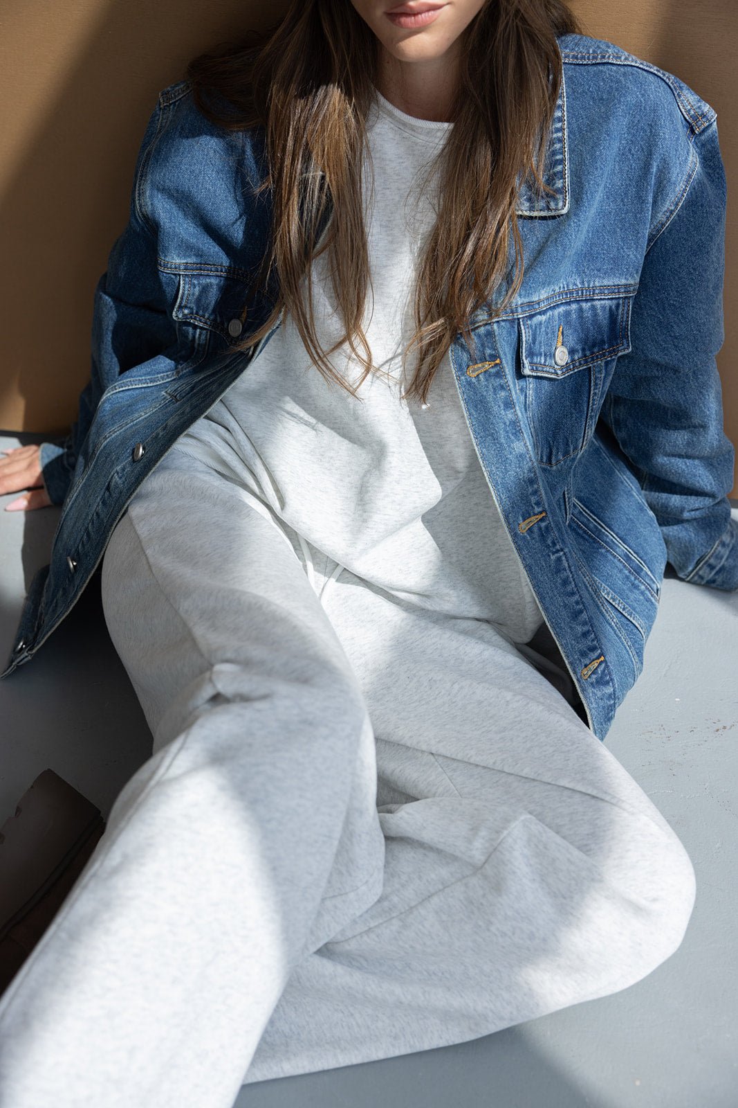 צעירה עם שיער חום לובשת ג'קט ג'ינס ומכנסי טרנינג אפורים, סטייל אופנת רחוב לנשים