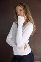 דוגמנית עם שיער גלי לובשת חולצת נשים לבנה עם שרוולים ארוכים ומכנסי ג'ינס כהים, צילום אופנה עדכני