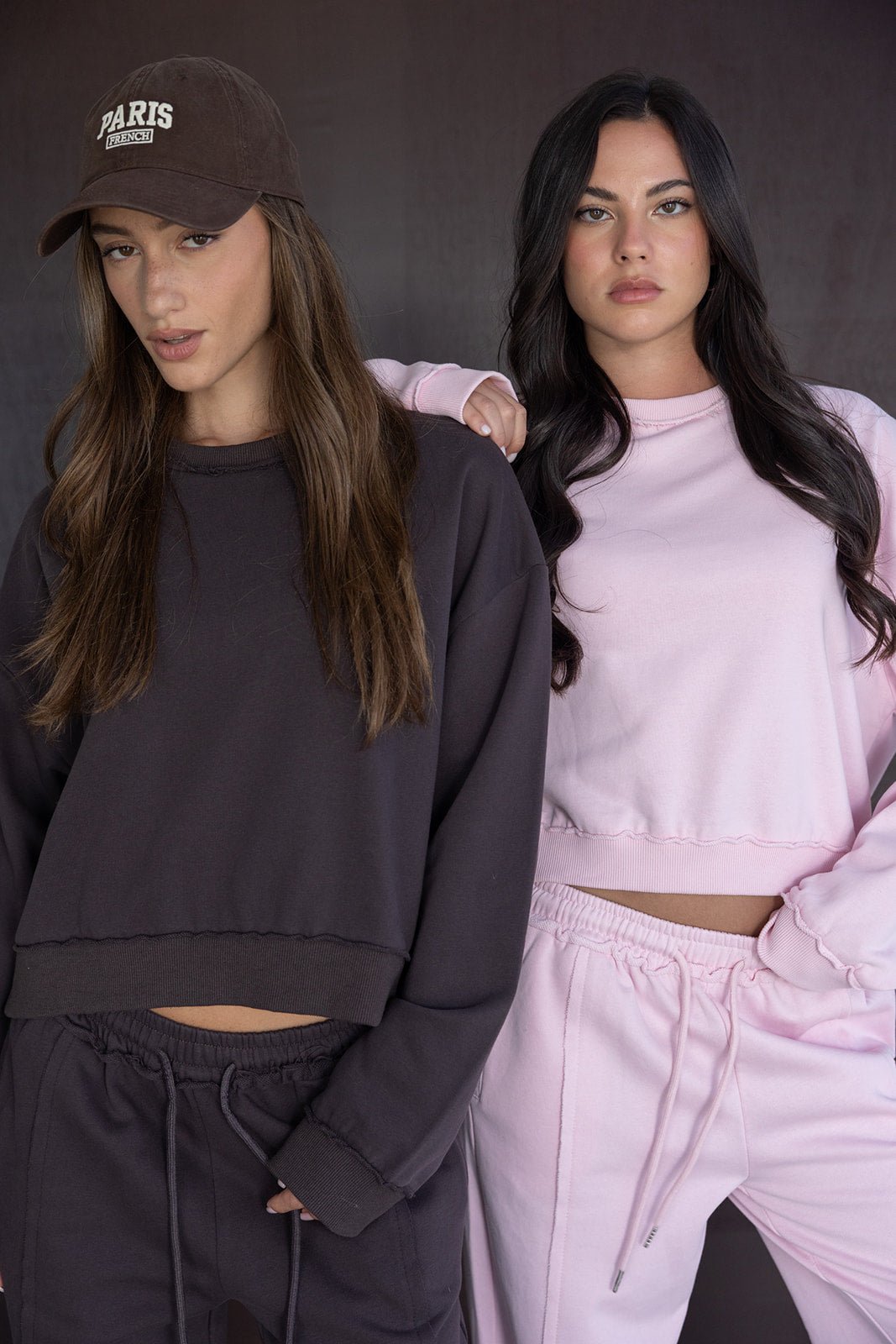 שתי נשים צעירות בלבוש קז'ואל, אחת בטרנינג שחור וכובע, השנייה בטרנינג ורוד בהיר, אופנת רחוב לנשים