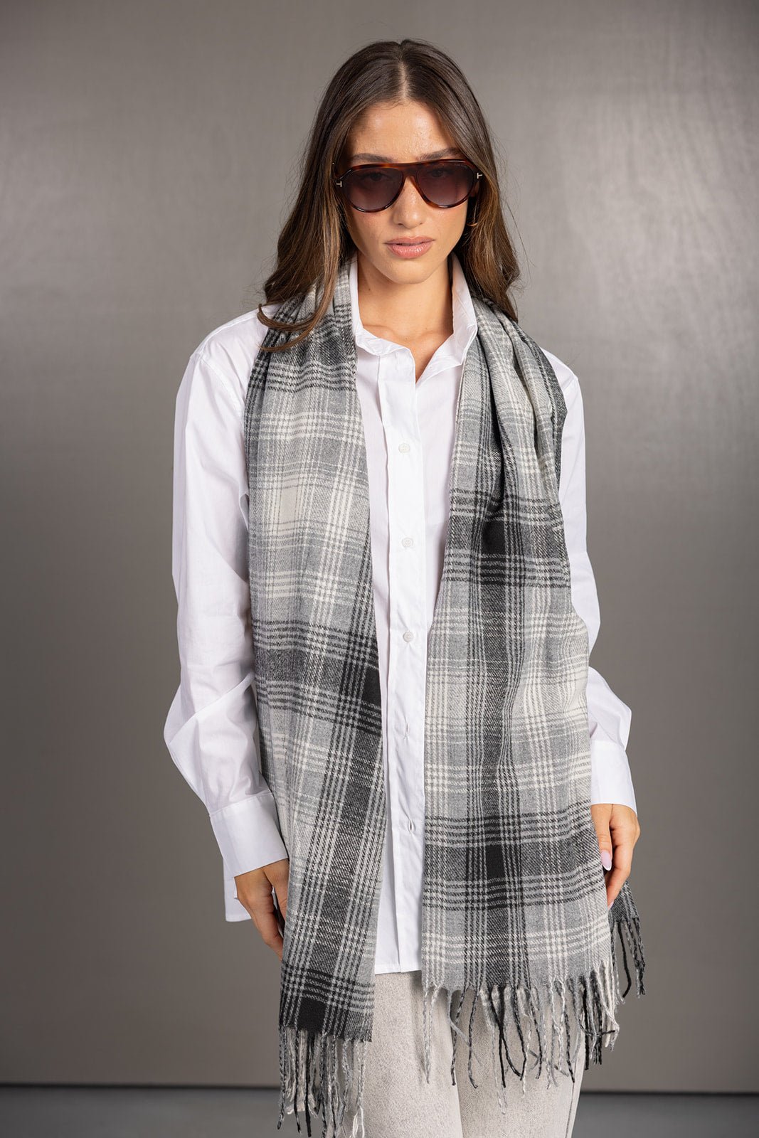 אישה לובשת חולצה לבנה צעירה עם צעיף משבצות אפור שחור ומשקפי שמש, אופנה נשית חורפית