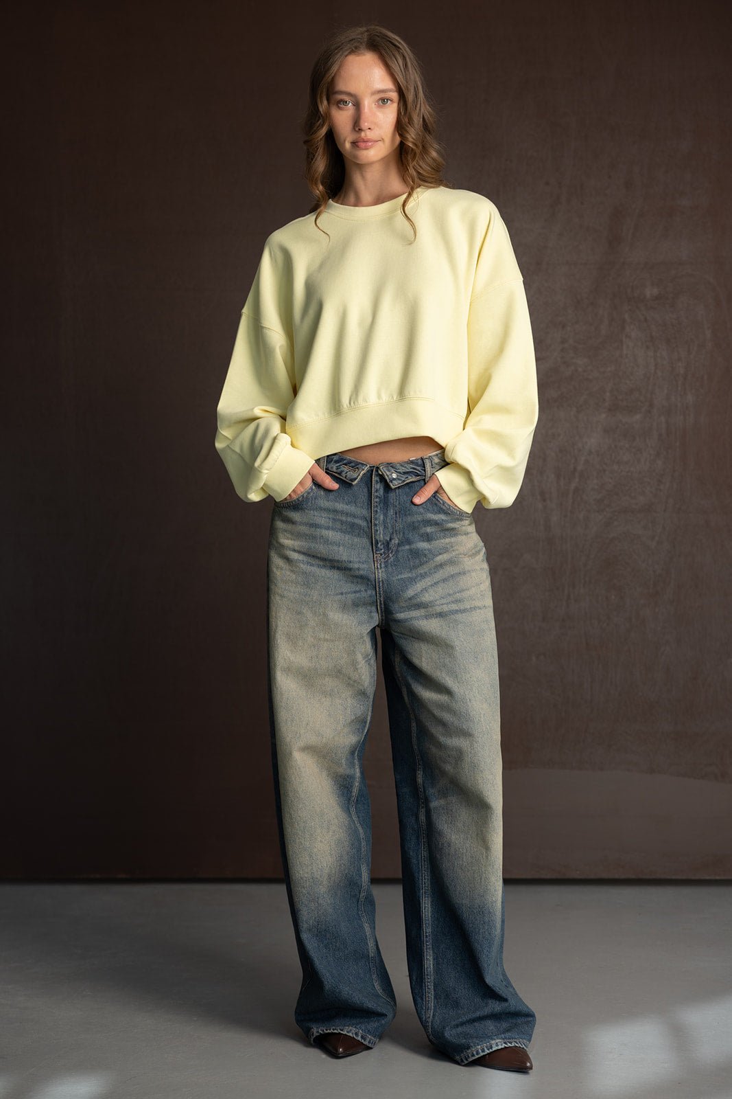 אישה לובשת סווטשירט צהוב קרופ ומכנסי ג'ינס רחבים באופנת רחוב לנשים