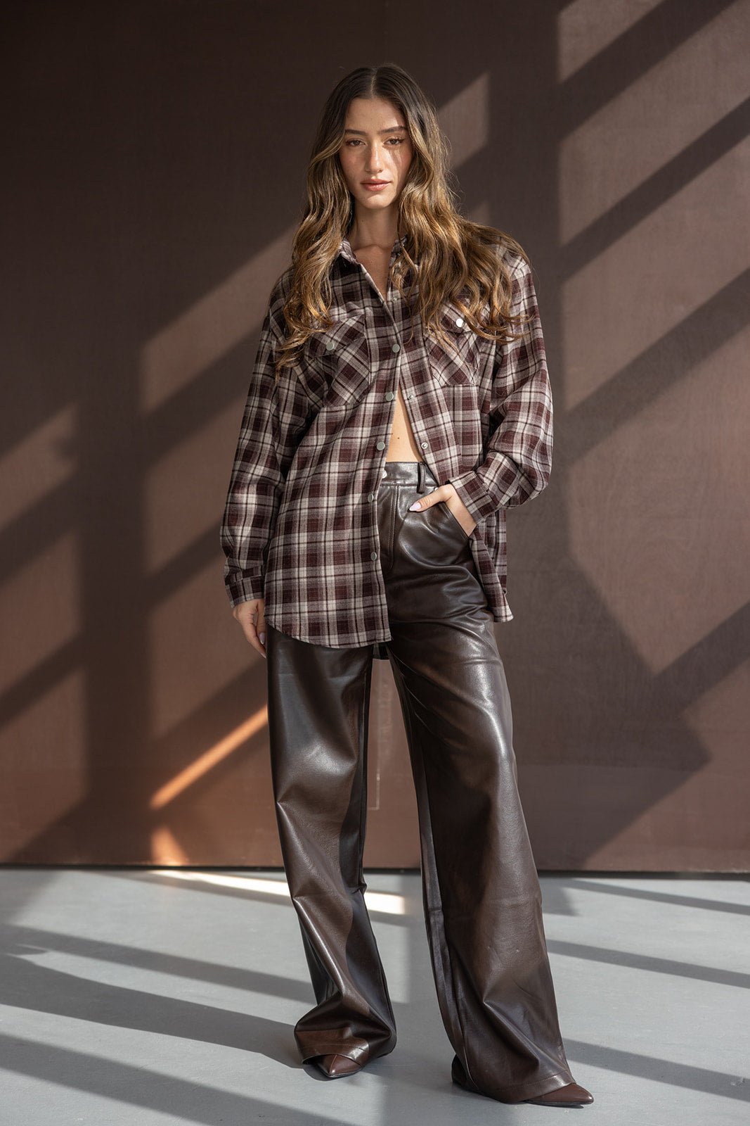 אישה עם חולצת פלאנל משובצת בצבע חום ומכנסי עור חומים, אופנת נשים עדכנית לצעירות