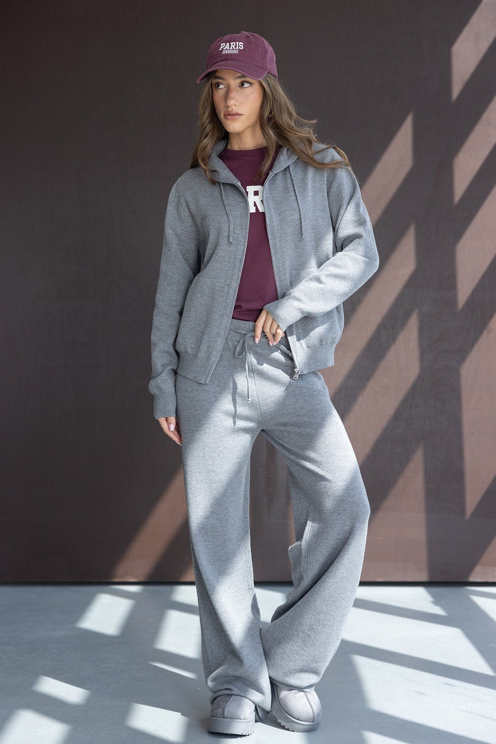 דוגמנית לובשת טרנינג אפור עם קפוצ׳ון, חולצת טי בורדו וכובע מצחייה, אופנת רחוב לנשים