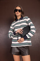 אישה עם חולצת פסים ארוכה, שורט עור שחור, תיק קלאץ' קלוע ומשקפי שמש אופנתיים