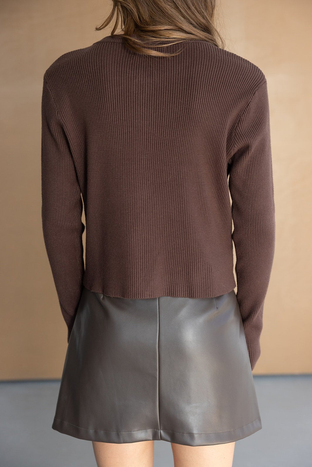 חצאית קצרה דמוי עור בצבע חום כהה עם סוודר חום ארוך, צילום גב, אופנת נשים