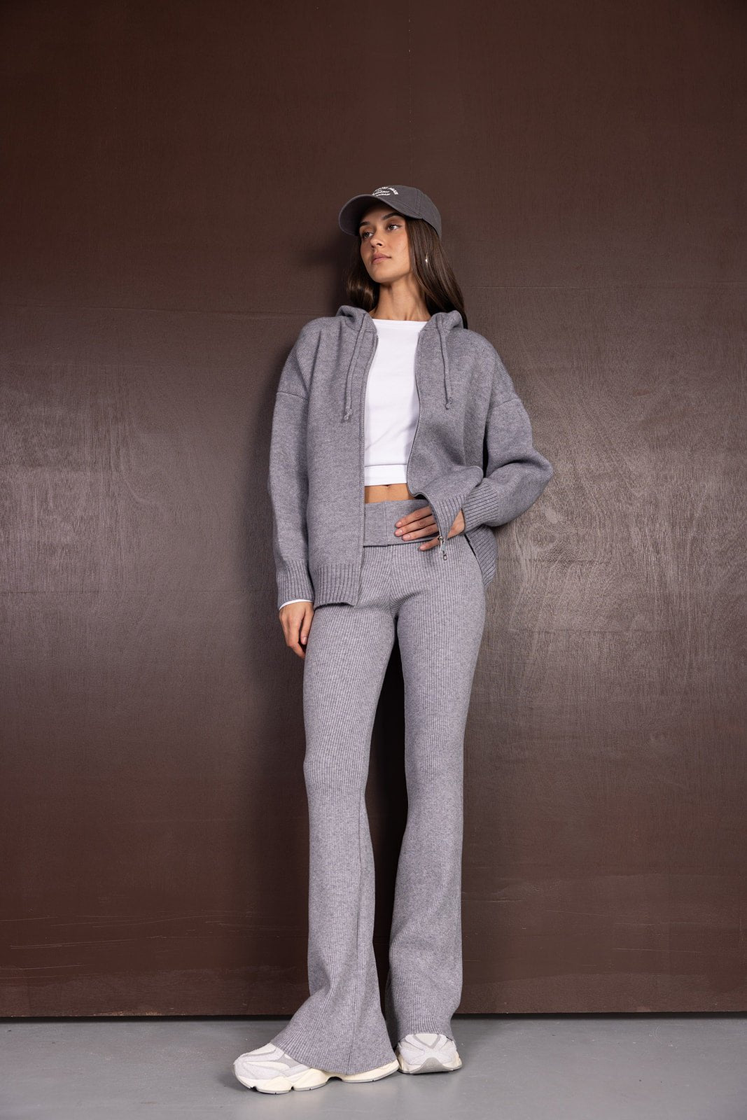 אישה לובשת סט סריג אפור עם קפוצ'ון, טי שירט לבנה וכובע מצחייה, אופנה יומיומית לנשים