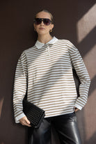 אישה עם חולצת פסים ארוכה, מכנסי עור שחורים, משקפי שמש ותיק קלאץ' שחור – אופנת נשים טרנדית