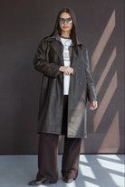 אשה עם מעיל עור חום, משקפי שמש, חולצת טריקו ומכנסיים רחבים באופנת חורף לנשים