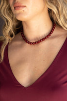 שרשרת חרוזים עגולים אדומים על אישה עם שמלת וי בורדו, אופנה לנשים