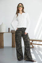 אישה עם מכנסי קארגו צבאיים רחבים, חולצת כפתורים לבנה ומשקפי שמש אופנתיים, בסגנון קז'ואל צעיר