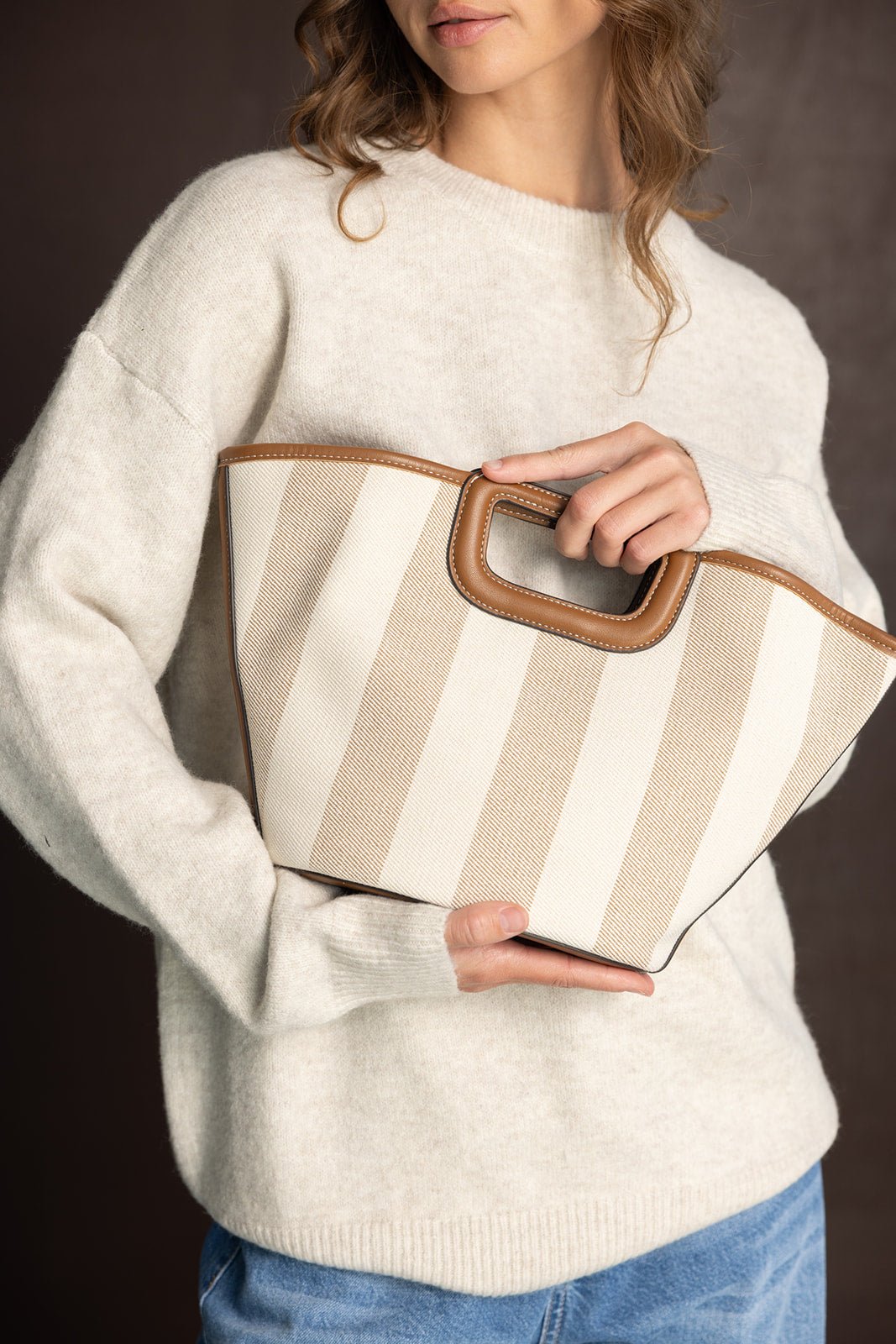 אישה עם סוודר בז' מחזיקה תיק יד בד פסים בז' ולבן, אופנה לנשים צעירות