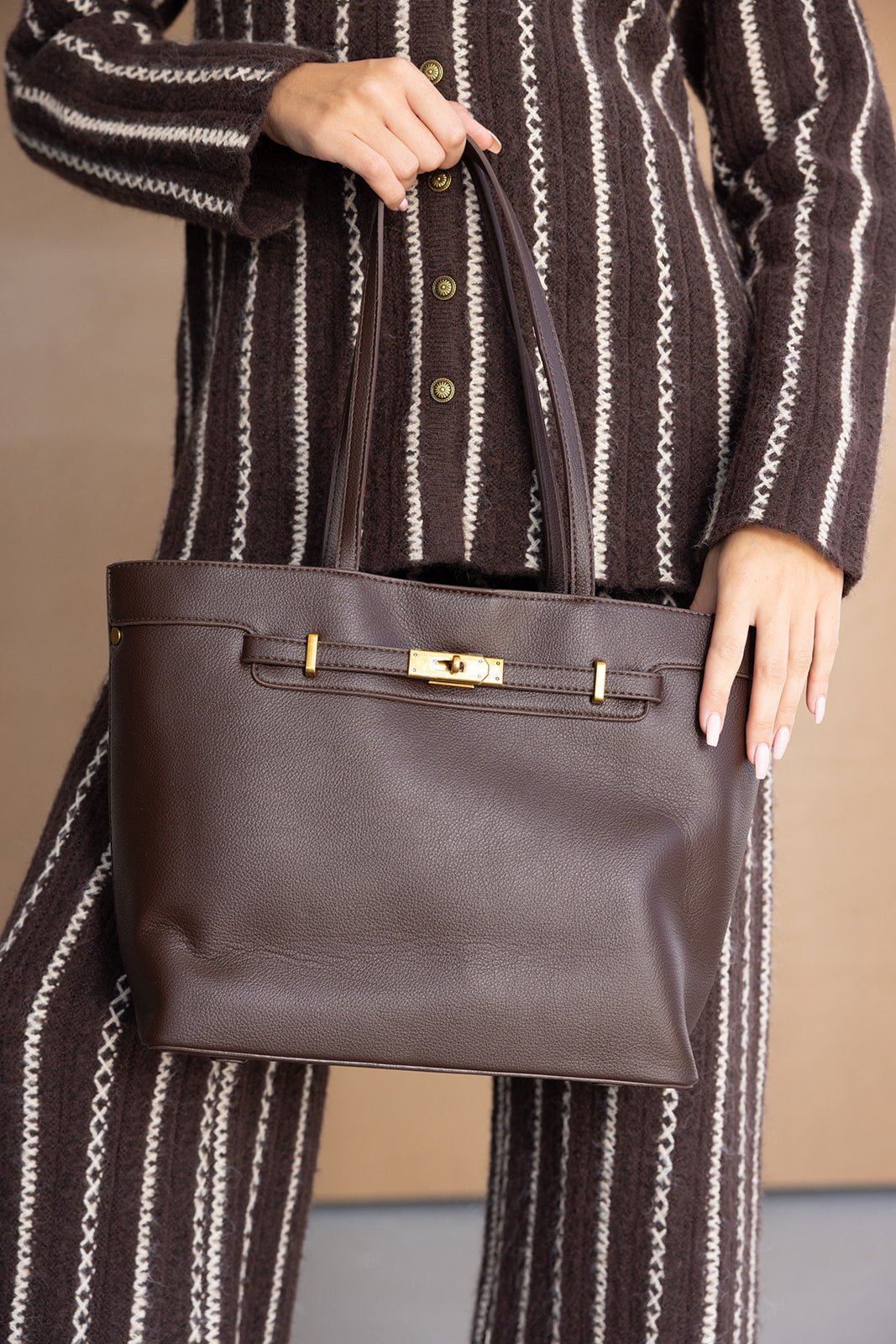 תיק יד חום לנשים מעור עם אבזם זהב, משולב עם חליפת פסים חומה ולבנה