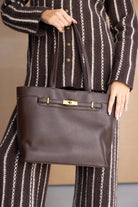 תיק יד חום לנשים מעור עם אבזם זהב, משולב עם חליפת פסים חומה ולבנה