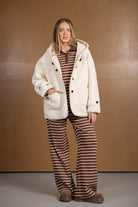 אישה עם בלונד שיער לובשת מעיל פליז שמנת ומכנסיים רחבים מפוספסים חום-לבן, בגדי חורף אופנתיים לנשים