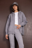 אישה לובשת סט קז'ואל אפור סרוג הכולל קפוצ'ון, מכנסיים בגזרה גבוהה וכובע מצחיה, לוק חורפי אופנתי לנשים