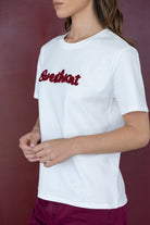 דוגמנית עם חולצת טי שירט לבנה כיתוב אדום ובגדי נשים אופנתיים, רקע בורדו