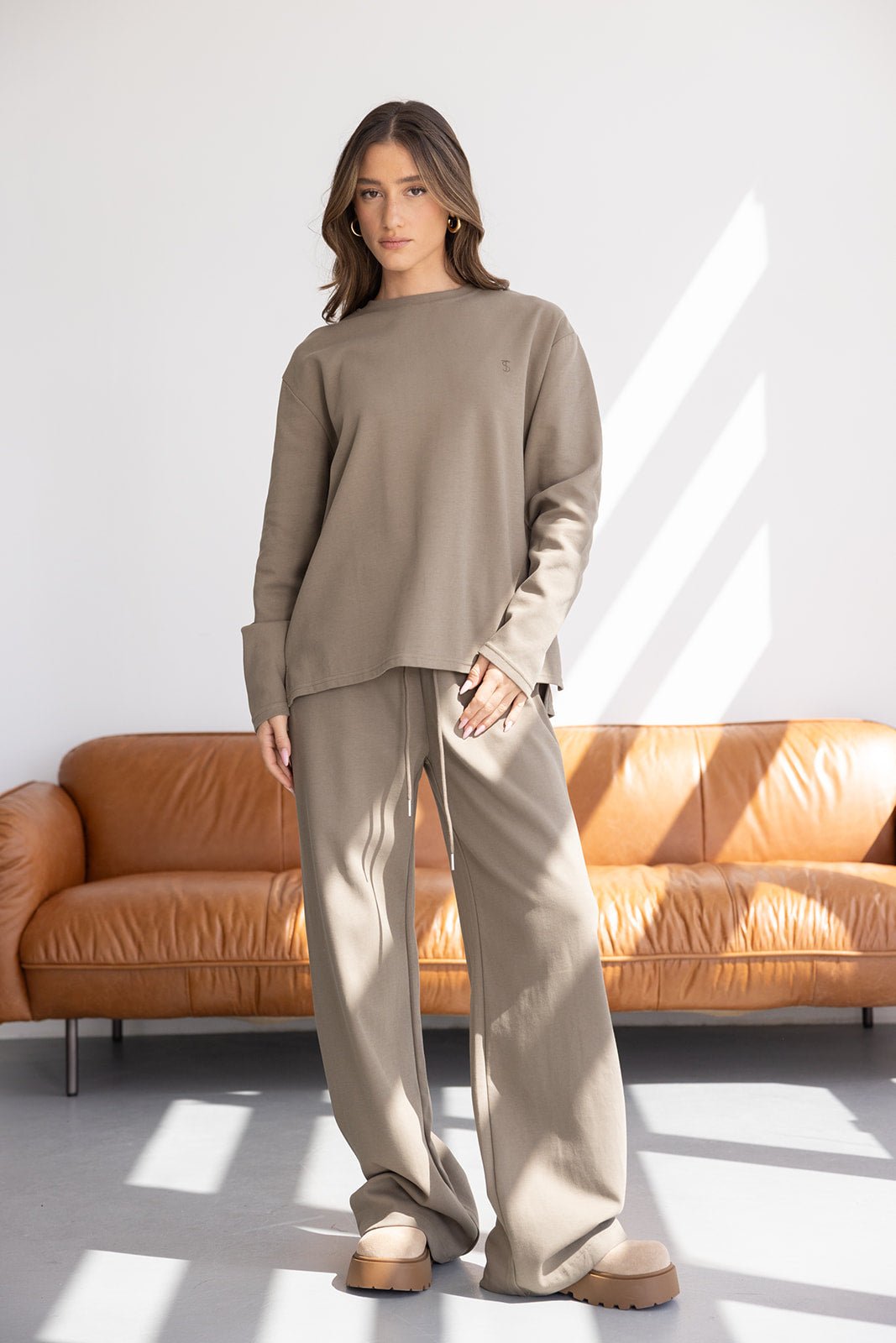 דוגמנית לובשת סט טרנינג נשים בגוון בז' מחויט, חולצה רחבה ומכנסיים מתרחבים, אופנת נשים עדכנית