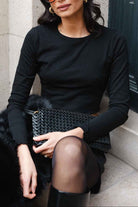 אישה יושבת עם חולצת שרוול ארוך שחורה, חצאית שחורה, תיק שחור קלוע ומשקפי שמש אופנתיים