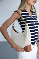 אישה לובשת חולצה מפוספסת מחזיקה תיק כתף בד שמנת עם רצועת עור חאקי ואבזמים מוזהבים, אופנת קיץ לנשים.