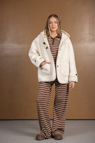 אישה לובשת ג'קט פליז לבן עם קפוצ'ון מעל סט פסים חום ולבן, אופנת חורף לנשים