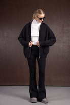 אישה לובשת סוודר רחב שחור, מכנסיים מחמיאים שחורים, טופ גולף לבן ומשקפי שמש אופנתיים