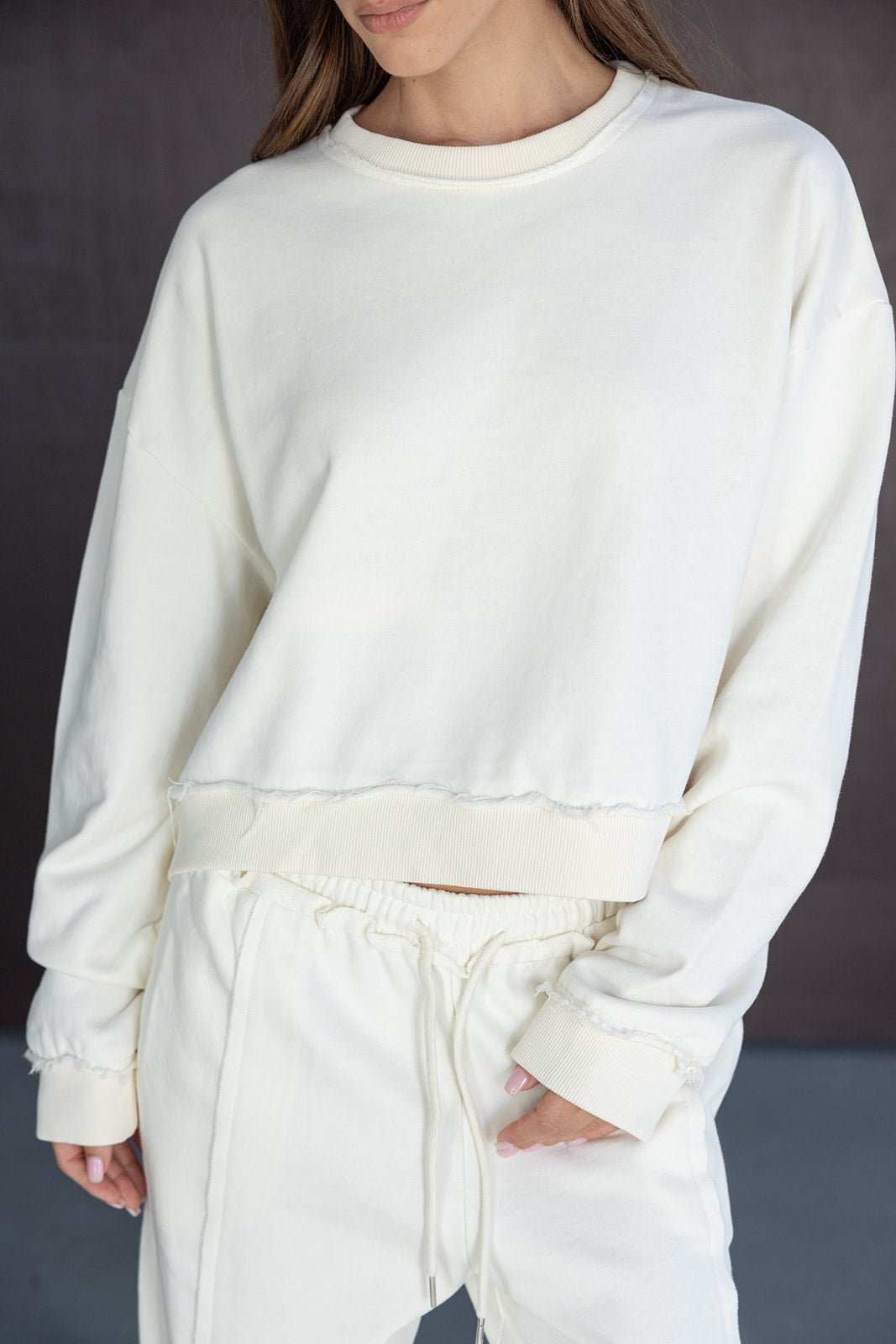 אישה לובשת סט טרנינג אופנתי בצבע לבן, סווטשירט עם קצוות גזורות ומכנסיים תואמים.